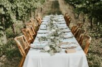 a neutral vineyard wedding reception with neutral linens, a greenery runner with white blooms and a lovely view of the vines