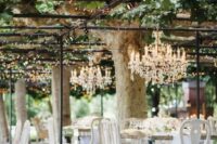 a neutral vintage wedding reception with mirror tables and white vintage chairs, crystal chandeliers over the tables and neutral blooms
