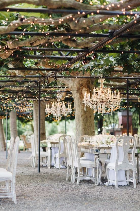 a neutral vintage wedding reception with mirror tables and white vintage chairs, crystal chandeliers over the tables and neutral blooms