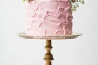 a pale pink textural buttercream wedding cake topped with greenery and some pink blooms is a pretty and delicate dessert for a spring wedding