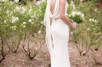 a plain sheath wedding dress with a cowl back, a sash, a train and a veil for a chic and romantic look