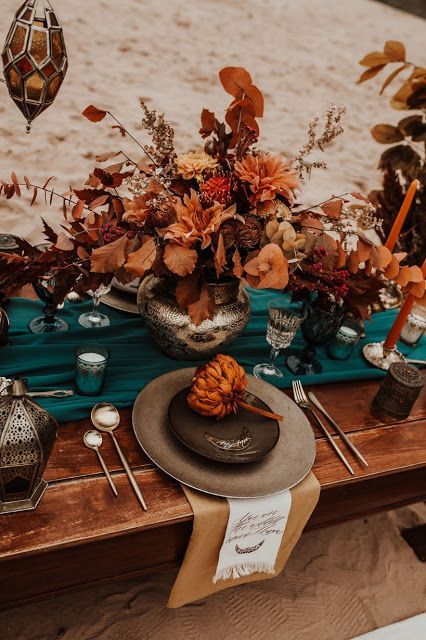 a refined boho beach wedding reception with rust and orange blooms, leaves and bold blooms on the table, with a teal runner