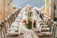 a refined vineyard wedding table setting with a neutral table runner, pink and coral blooms and greenery and crystal chandeliers over the space