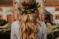 a romantic boho wedding hairstyle with a twisted and braided halo with a volume on top and waves plus leaves