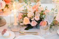 a romantic peach and blush wedding tablescape with blush and peachy blooms, orange napkins, gold cutlery and greenery plus tall candles