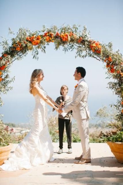a round wedding arch covered with greenery and orange blooms is a great idea not ony for a beach but also for many other weddings