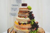a rustic display with grapes, figs, straw and toppers on a large cheese wheel tower and on an oversized wooden slice