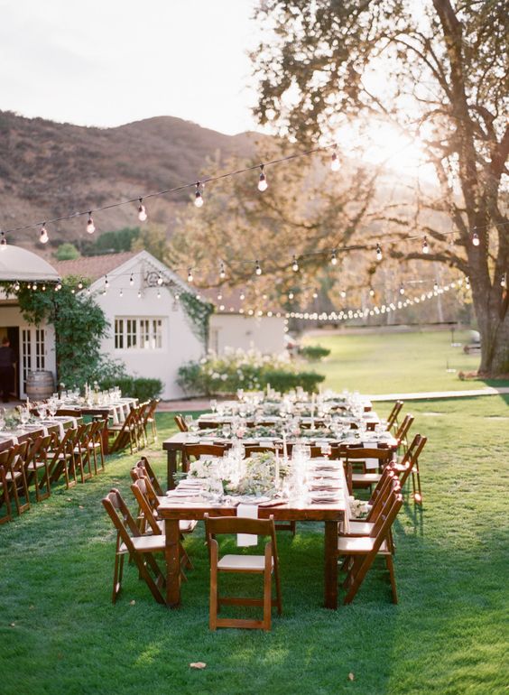a rustic wedding reception with stained tables and chairs, greenery and candles and string lights over the reception space