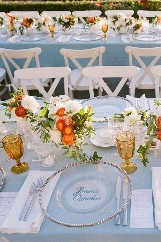 a seaside tablescape with a blus tablecloth, white and orange blooms, amber glasses and greenery plus candles is amazing