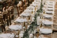 a stylish rustic wedding reception space with stained tables, a greenery table runner, pillar candles and oil bottles as favors