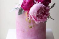 a trendy white and watercolor pink wedding cake with fuchsia and light peonies plus pale leaves and gold leaf