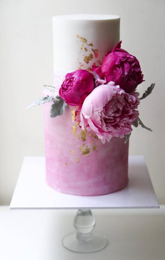 a trendy white and watercolor pink wedding cake with fuchsia and light peonies plus pale leaves and gold leaf