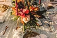 a tropical beach wedding tablescape with neutral linens, a pink and orange centerpiece with fronds and pink candles is wow