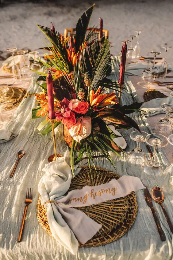 a tropical beach wedding tablescape with neutral linens, a pink and orange centerpiece with fronds and pink candles is wow