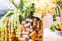 a vase filled with wine corks and white flowers and greenery in it for a vineyard wedding