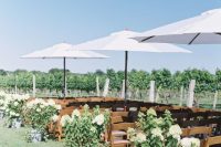 a vineyard wedding ceremony space with white floral arrangements and greenery, white umbrellas