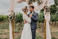 a wedding arch placed right in the vines, with pastel pink fabroc, neutral and blush blooms is a lovely idea for a vineyard wedding
