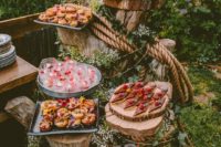 a wedding dessert display of tree stumps decorated with greenery, blooms and ropes and wood slices as sweets stands