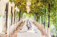 a wonderful vineyard wedding reception with vines, curtains, crystal chandeliers, neutral linens and chair covers plus lilac blooms