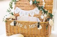 a woven suitcase decorated with greenery, white blooms and banners is a gorgeous idea for a rustic or just relaxed wedding