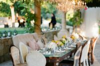 an eclectic vintage vineyard wedding reception with a dark-stained table, neutral chairs and a loveseat, crystal chandeliers and yellow blooms