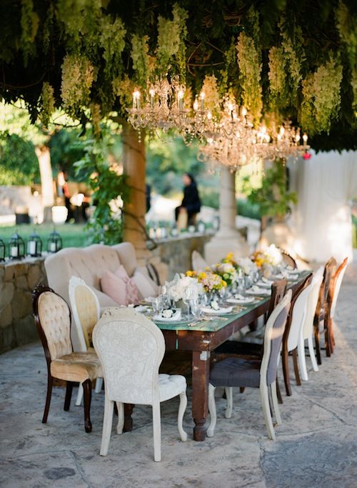 an eclectic vintage vineyard wedding reception with a dark-stained table, neutral chairs and a loveseat, crystal chandeliers and yellow blooms