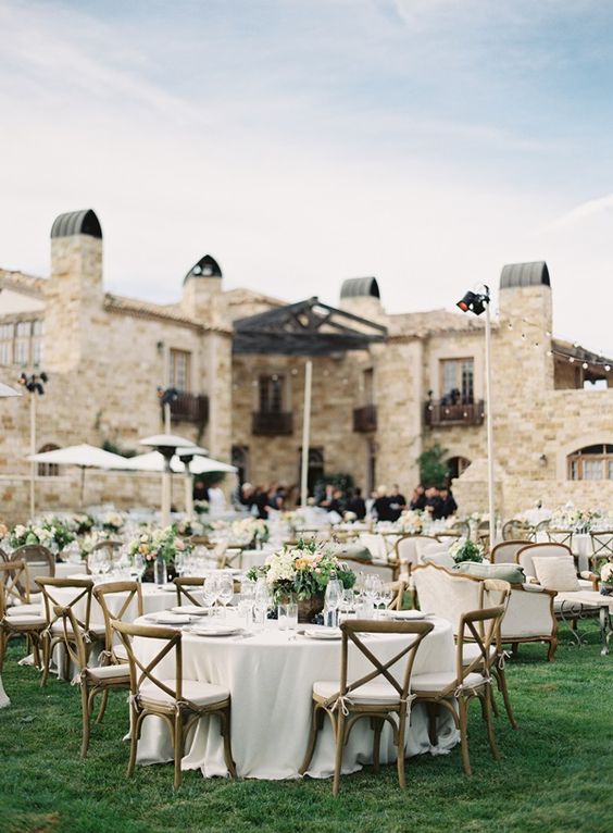 an elegant neutral wedding reception space with neutral linens and chairs, with neutral centerpieces and greenery and some string lights over the space