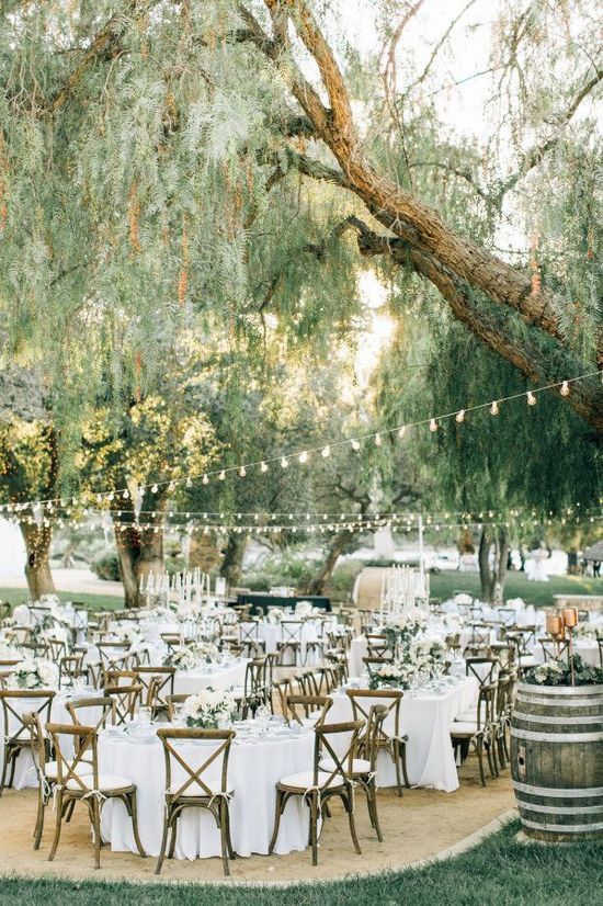 an elegant rustic wedding reception space with white tablescape and white blooms, some greenery and string lights over the space