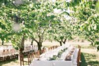 an elegant vineyard wedding reception with neutral linens, a greenery runner and potted greenery, tall and thin candles