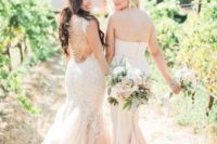 brides wearing blush mermaid wedidng dresses, one with chain back and white lace appliques, and the second of plain fabric and a layered tail