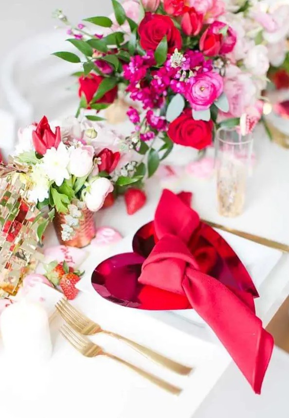 a beautiful Valentine wedding tablescape with pink heart chargers, gold cutlery, bold blooms and greenery