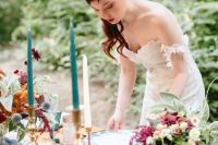 a beautiful and bright fall woodland wedding tablescape with layered runners, bold and blush blooms and greenery, turquoise candles and dark bottles