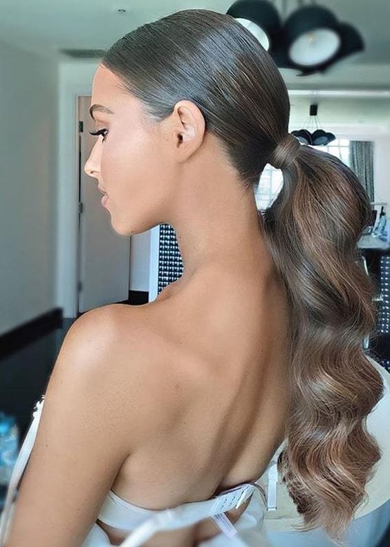 a beautiful and elegant wavy low ponytail with a sleek and shiny top is a stylsih idea for a glam bride