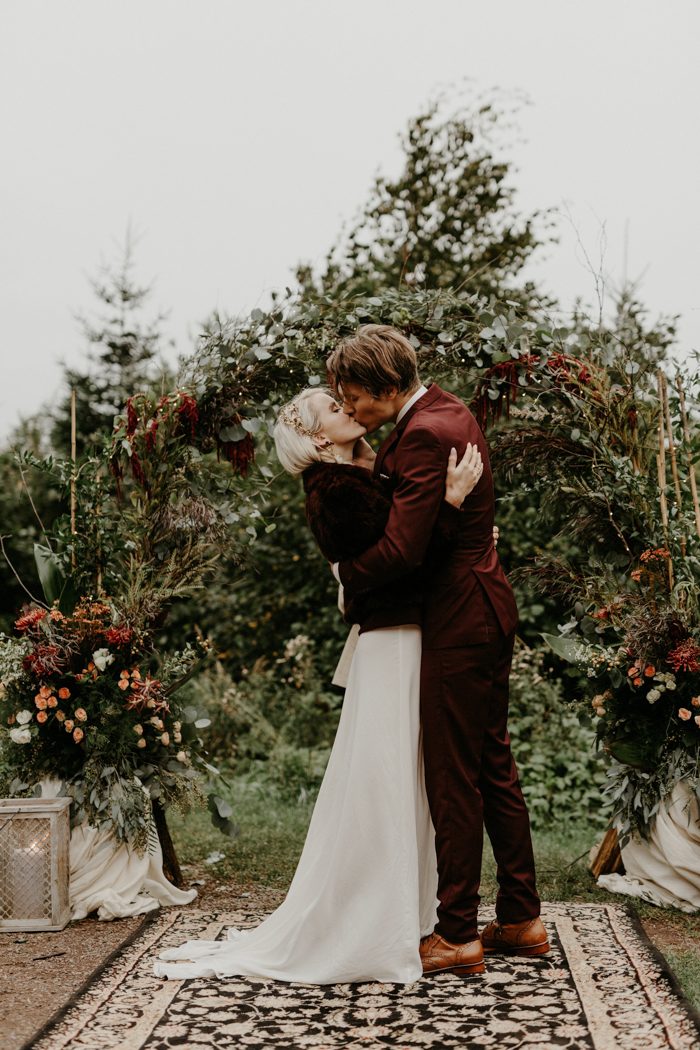 a beautiful fall woodland wedding arch covered with textural greenery and pinka nd burgundy blooms is pure chic