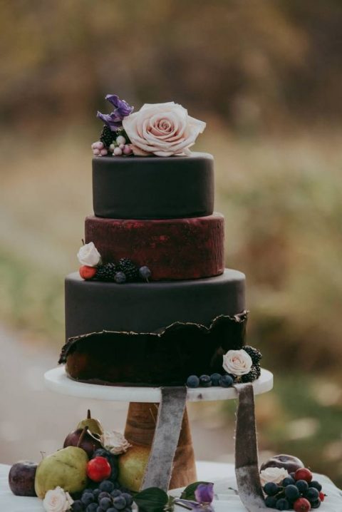 a black and burgundy wedding cake with berries and blush blooms for a modern and chic fall wedding with a touch of moody color