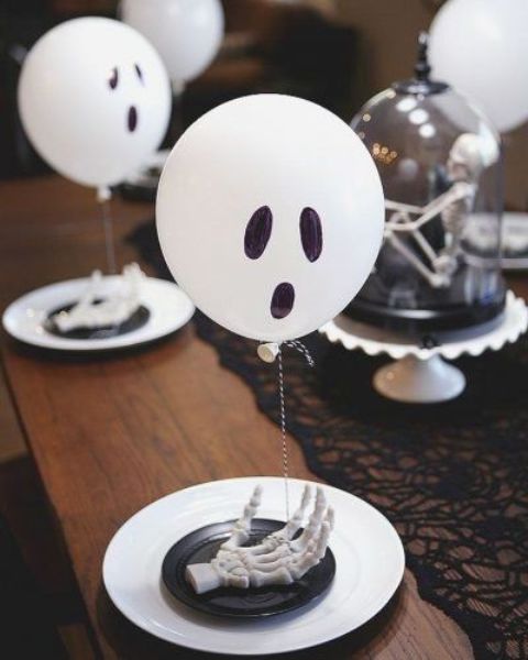 a black and white Halloween bridal shower tablescape spiced up with skeleton hands, white ghost balloons and a black lace runner