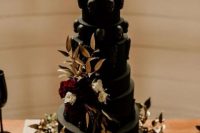 a black wedding cake with skulls on its tiers and a skull on top plus bold blooms and gilded foliage is a fantastic idea for a Halloween wedding