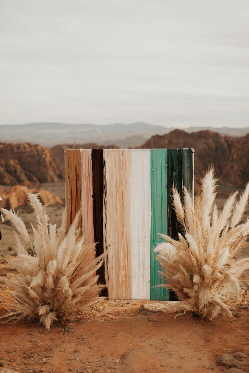 a bold boho fall wedidng backdrop of bright stripes and pampas grass arrangements is a cool and bright idea for a desert wedding