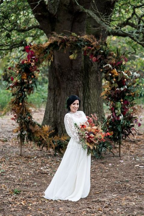 a bold fall wedding woodland wedding arch with leaves, greenery and blooms features plenty of texture and cool colors