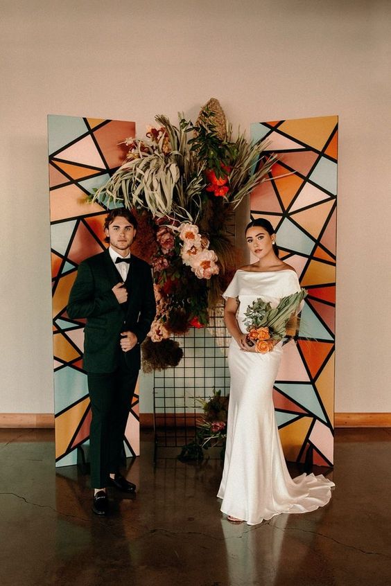 a bold geometric wedding backdrop with red, blush blooms, fronds and air plants is a bright and cool idea for a mid-century modern wedding
