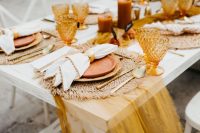 a bright and chic Thanksgiving wedding tablescape with a mustard runner, woven placemats, bold candles and blooms, colored glasses