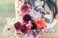 a bright fall wedding bouquet with lilac, orange and plum-colored blooms, greenery and leaves is a catchy solution to rock