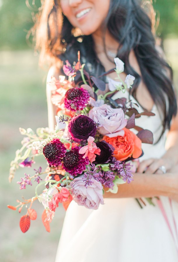 A bright fall wedding bouquet with lilac, orange and plum colored blooms, greenery and leaves is a catchy solution to rock