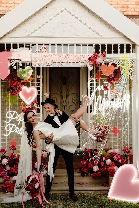 a bright wedidng backdrop with pink, red and white blooms, a neon heart and some more decor is a lovely and bright idea for a wedding
