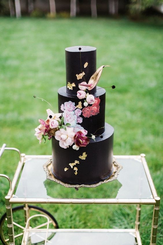 a catchy black wedding cake with pastel fresh blooms, gold leaf and twigs, painted blooms is a beautiful and artful idea for a wedding