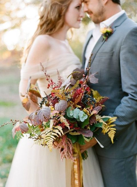 a chic fall woodland wedding bouquet with fall leaves, berries and branches done in burgundy and rust