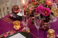a chic plum-colored tablescape with pink blooms and napkins, gold cutlery and candleholders, tall and thin candles
