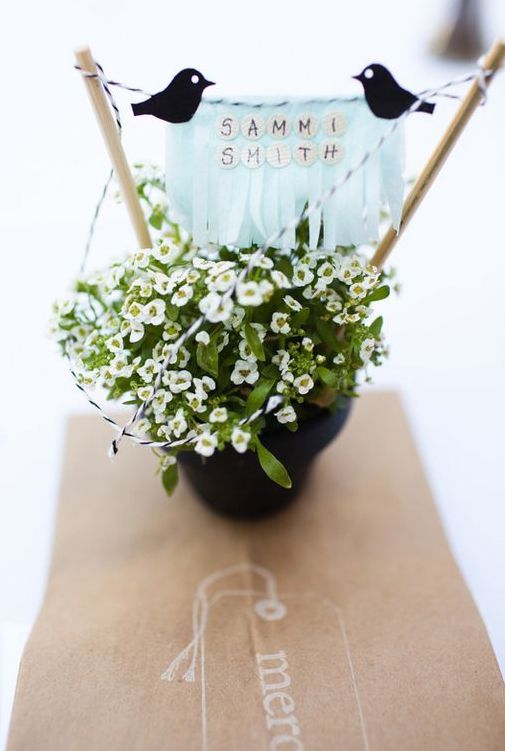 a cool wedding centerpiece of potted blooms, a stand with a banner, black birds is a pretty idea for a rustic wedding