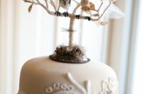 a crazy neutral wedding cake with a doily pattern, a tree with a couple of birds is very creative and fun