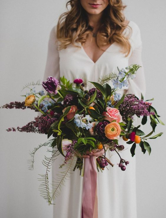 A dimensional and textural wedding bouquet with plum colored, blue and orange blooms, leaves and ferns is wow